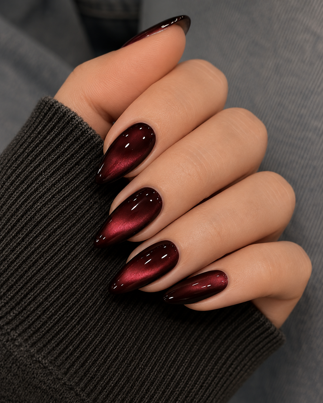 Deep burgundy almond nails featuring a velvet cat-eye magnetic effect, creating a shimmering 3D light-reflecting streak across the dark red base.