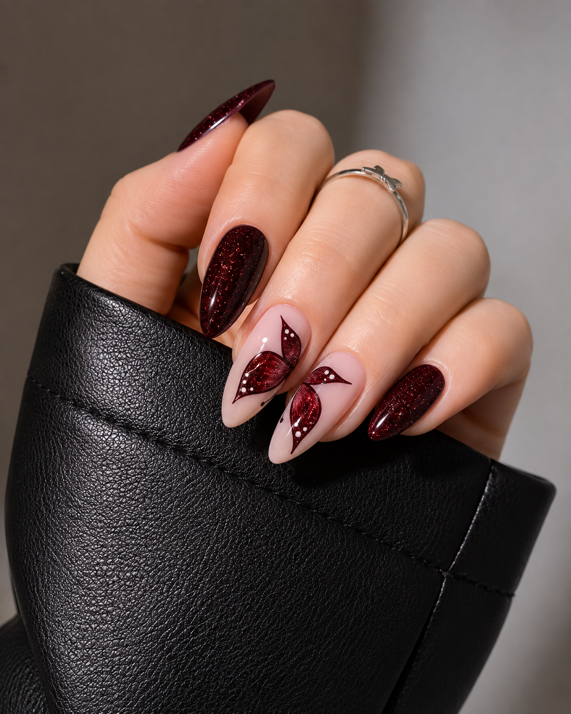 Almond-shaped nails featuring a deep burgundy vampy red glitter finish. The middle and ring fingers display a dark red glittery butterfly wing design on a translucent nude base, forming a complete butterfly when placed together.