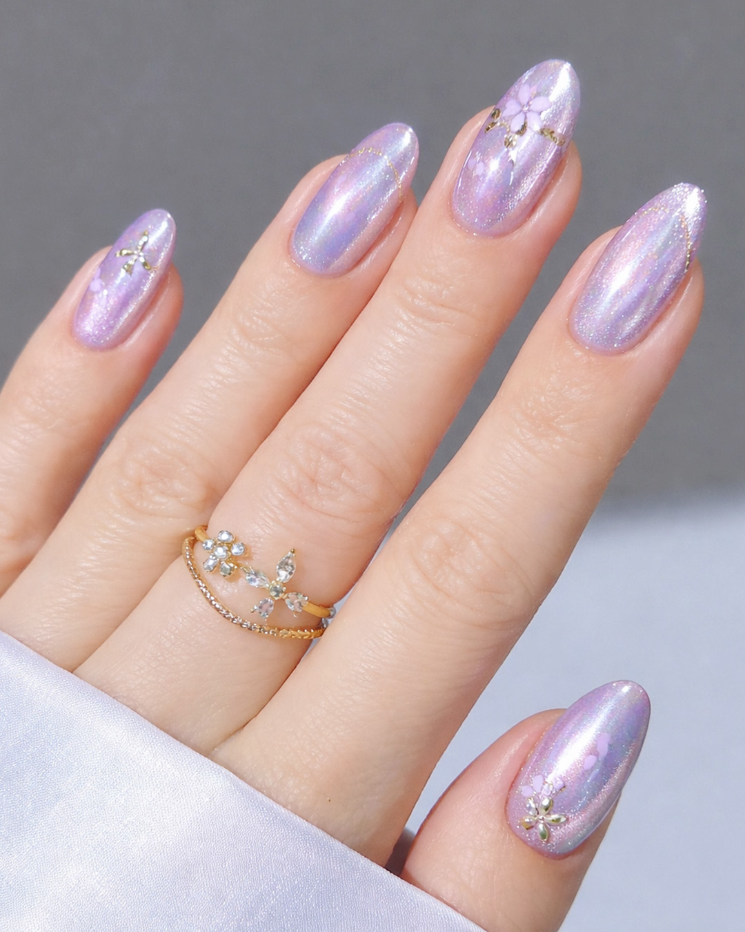 Lavender chrome almond nails with a shimmering finish, featuring small floral details and subtle gold accents.