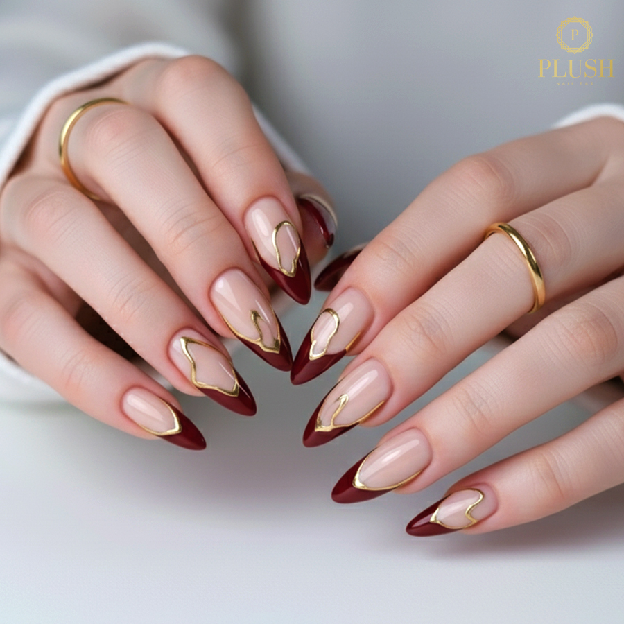 Deep garnet almond nails with gold-edged French tips, perfect for fall nail inspiration