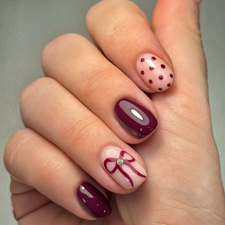 Short glossy Burgundy nails with subtle bow accent and minimalist nail art.