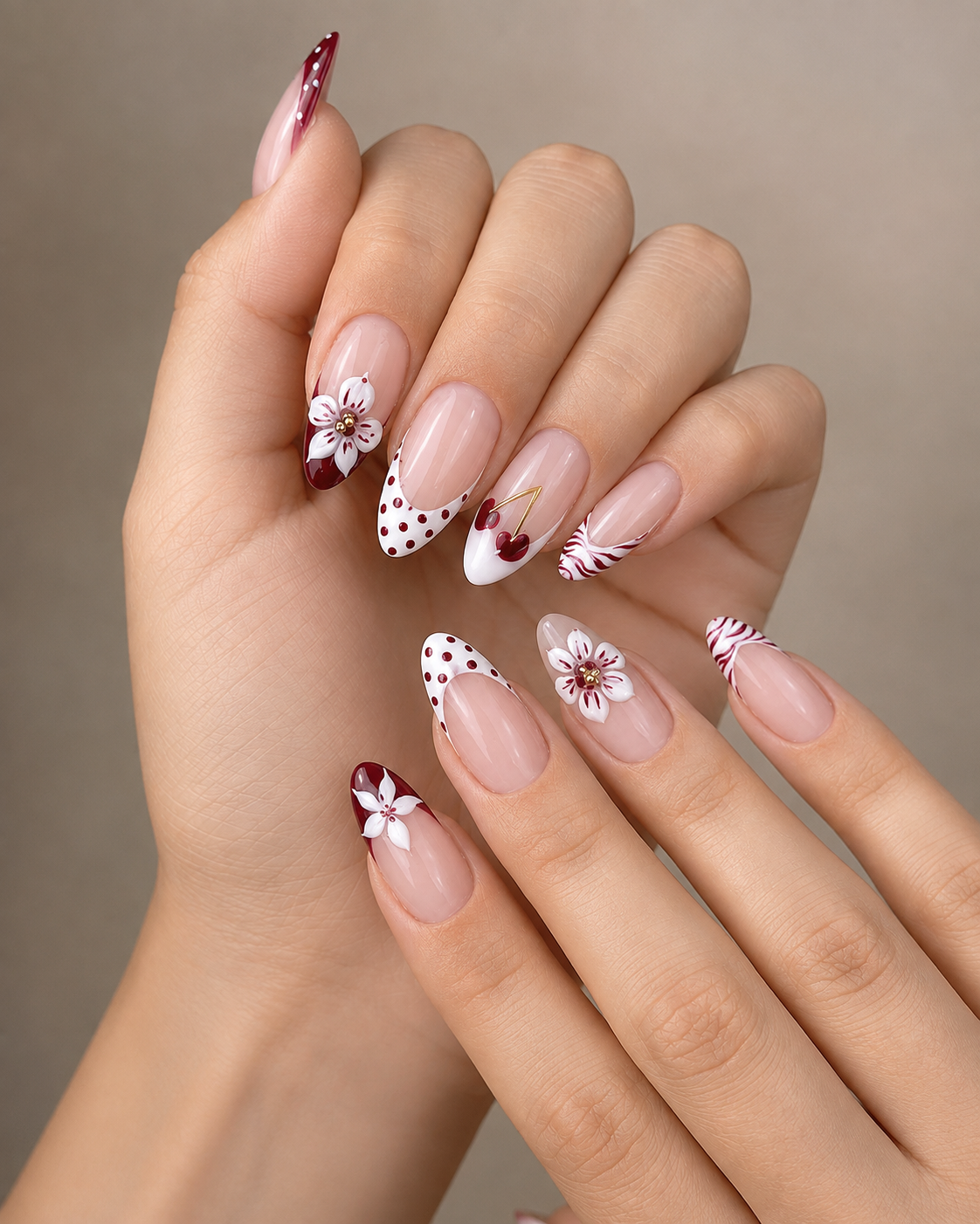 Almond nails featuring a creative French tip design in dark red and white polka dots. Decorated with 3D white flower accents with gold centers and a small pair of cherry nail art motifs.