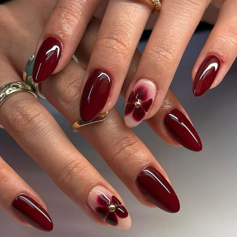Deep glossy Burgundy manicure featuring one floral accent nail, elegant autumn look.
