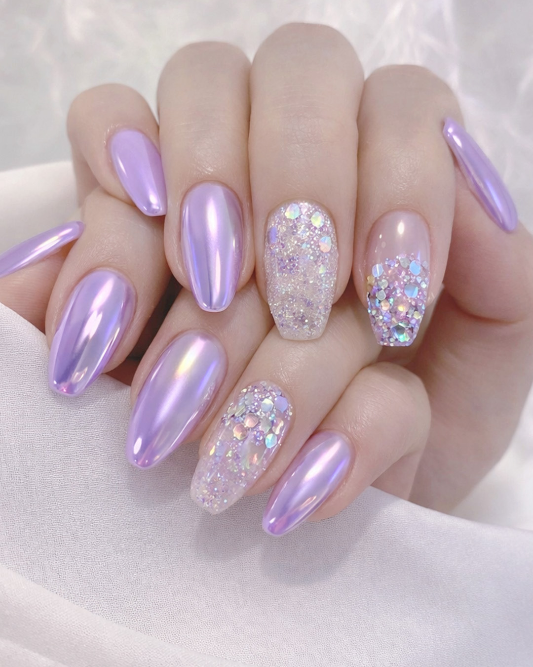 Lavender chrome nails with glossy finish paired with glitter accent nails featuring chunky sparkles and reflective elements.