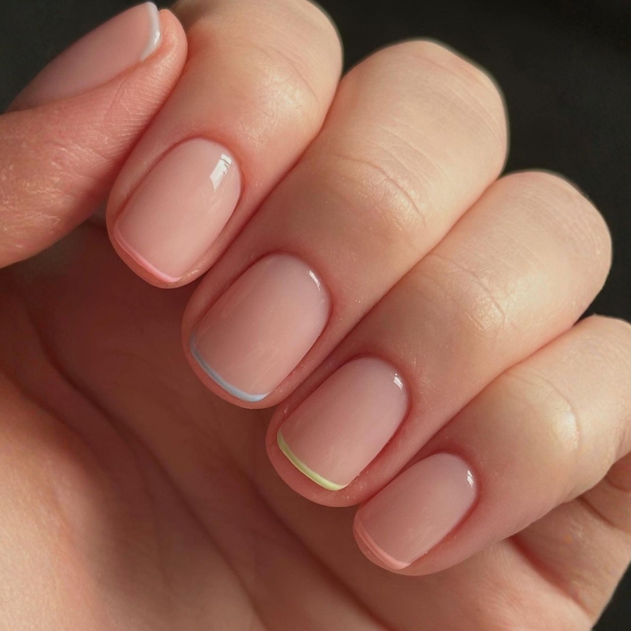 Fun and minimalist micro French tips in pastel rainbow colors on clean, short nude nails.