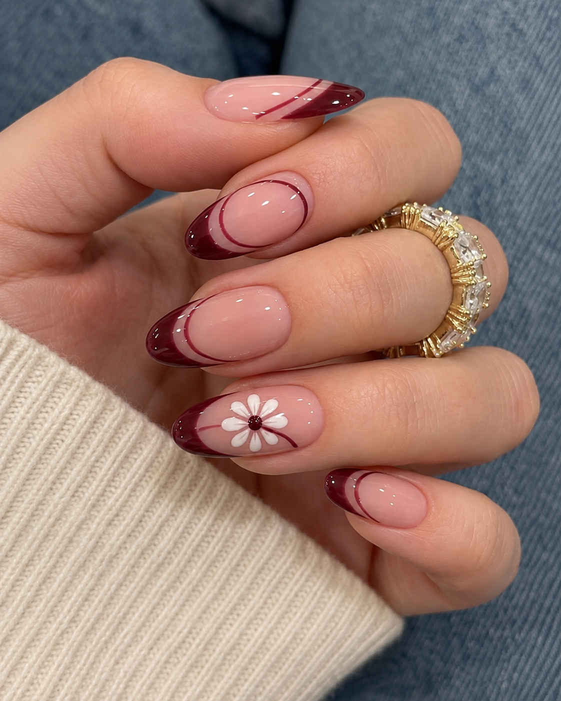 Double-lined French tip almond nails in a rich dark red color. Includes a subtle white daisy art accent on the ring finger with a burgundy center on a natural nude base.