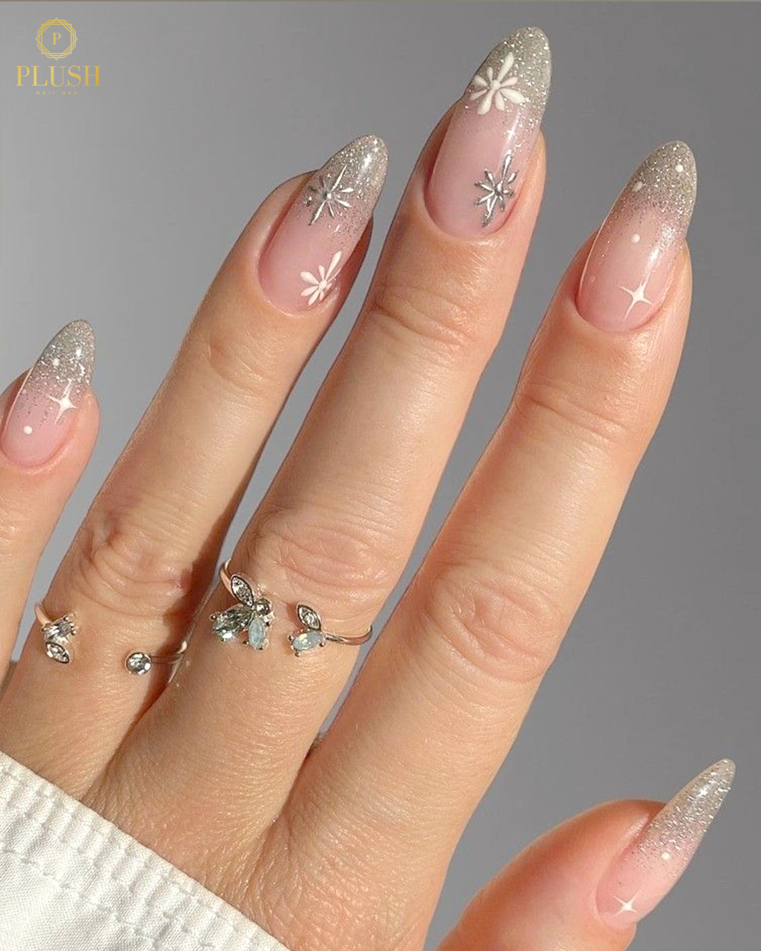 Soft pink almond nails with white glitter tips and detailed snowflake accents for a winter look.