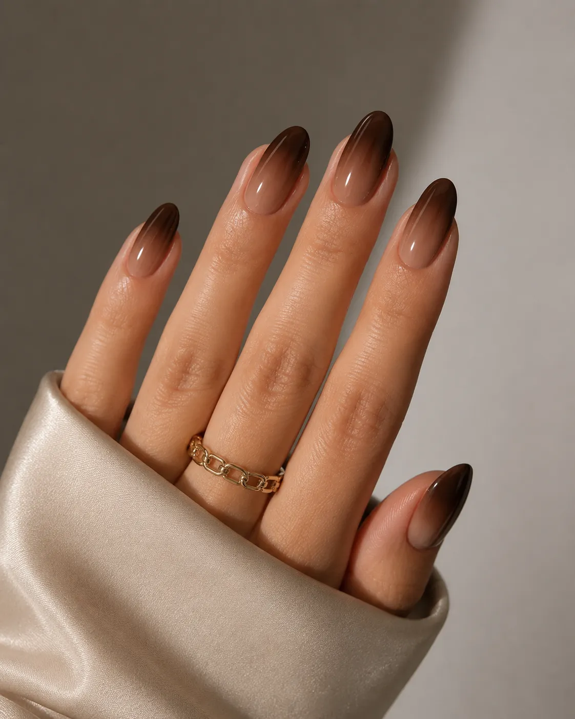 8 Ways to Wear Brown Nails This Season in Houston 6 Hand with long oval nails in brown ombre polish, wearing gold chain ring