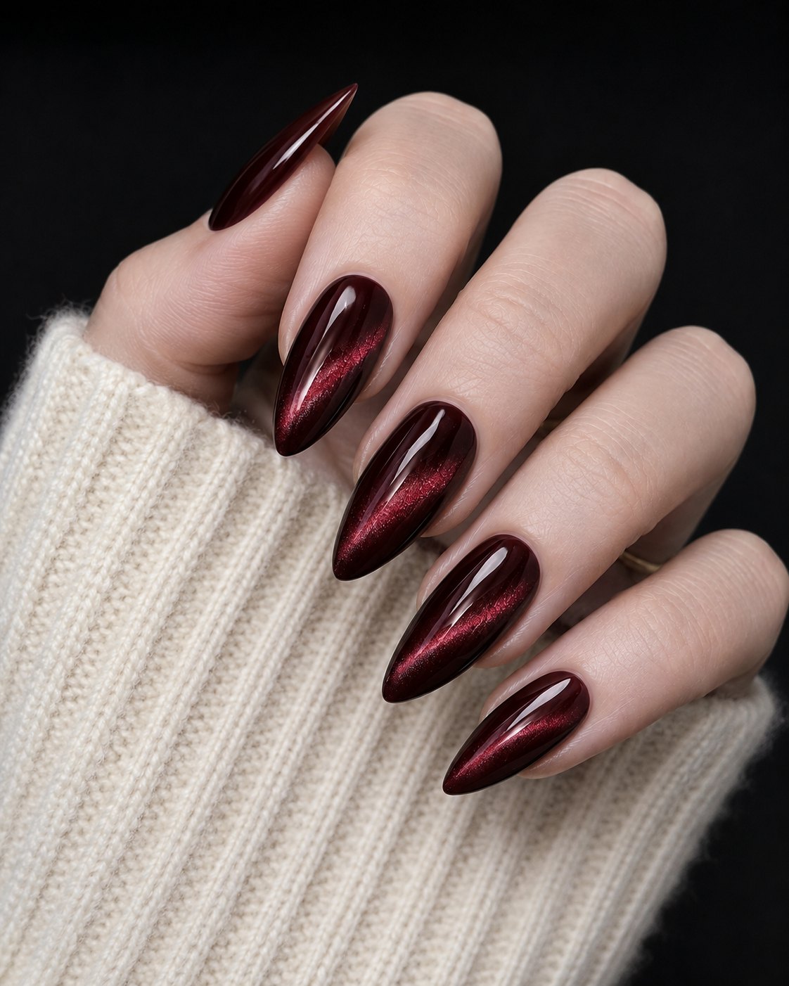 Long almond burgundy cat eye nails with a bright light streak down each nail on a black background