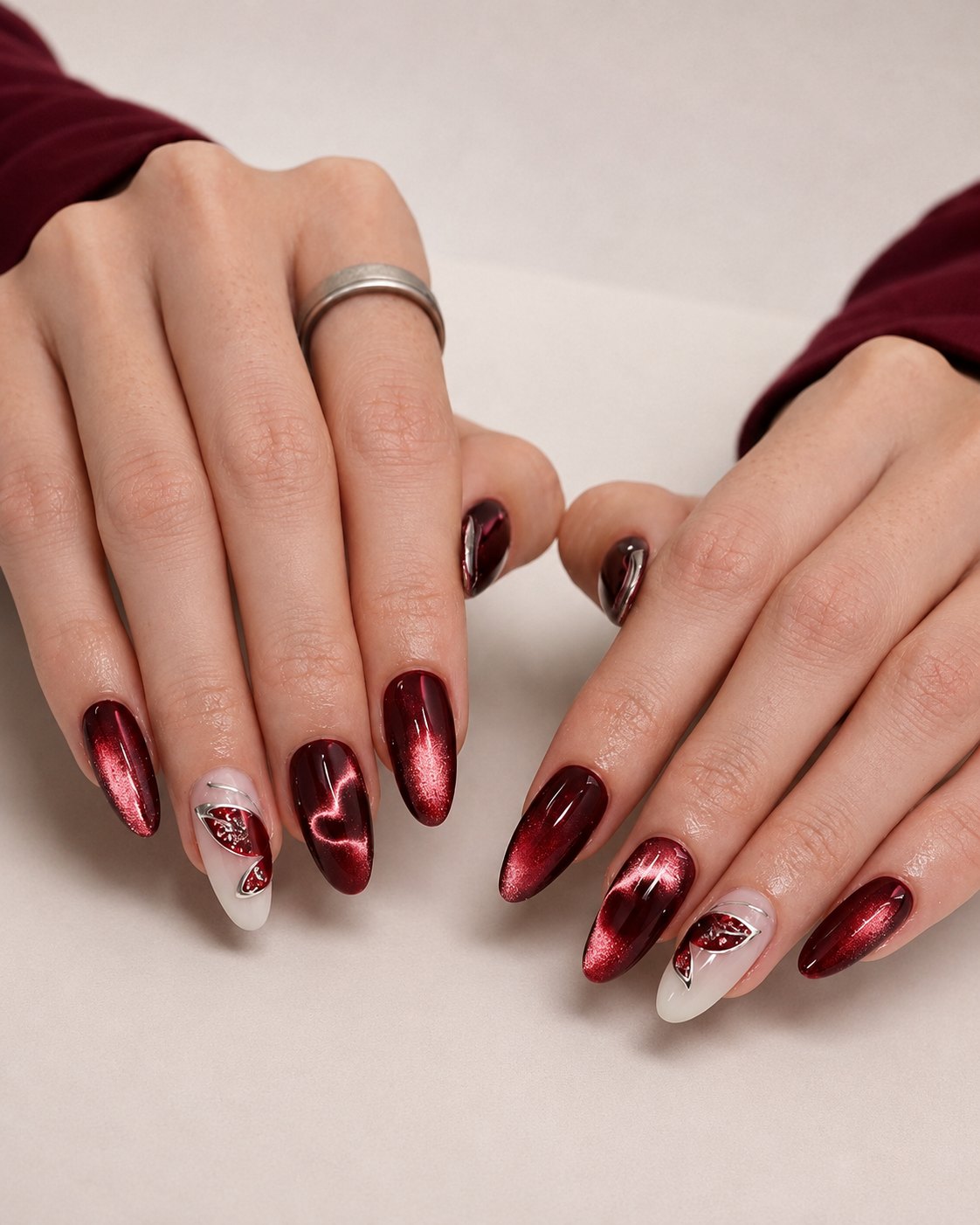 Burgundy cat eye nails with a curved magnet swirl beside milky white nails with painted leaf art