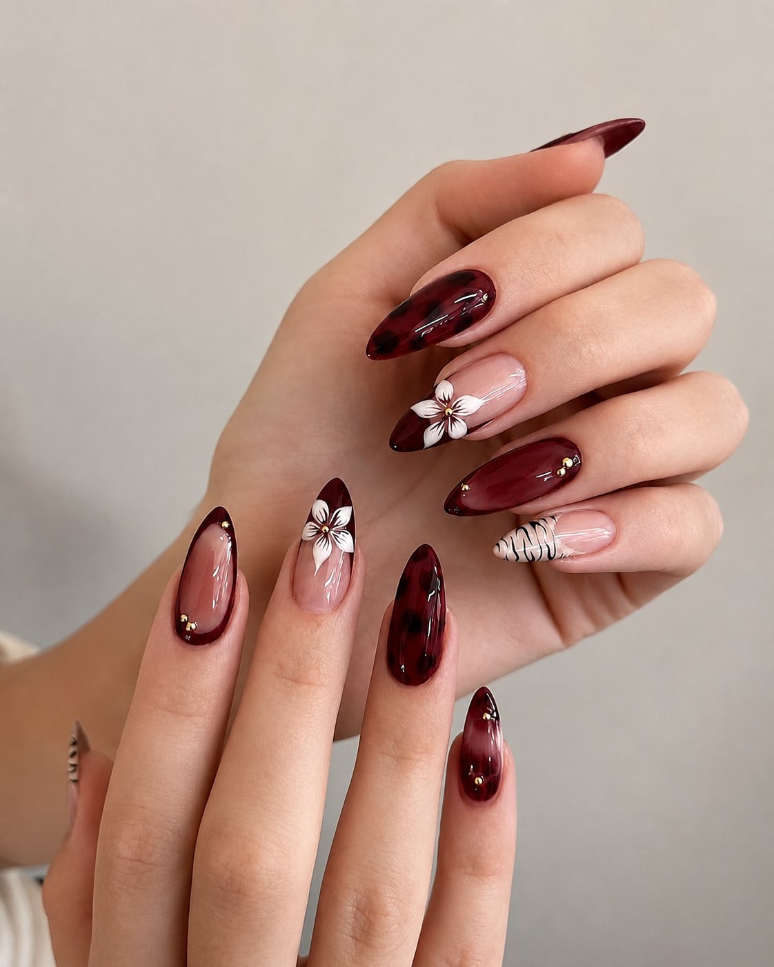 Burgundy tortoiseshell marble nails with sculpted white flowers and gold beads on translucent tips