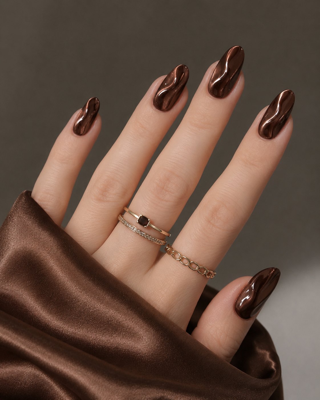 Chocolate brown chrome almond nails with raised glossy waves catching the light