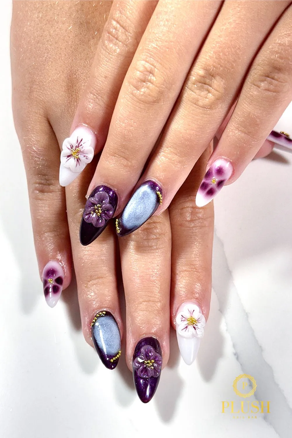 Elegant 3D floral nails with purple petals, white blossoms, and glossy ombre finishes