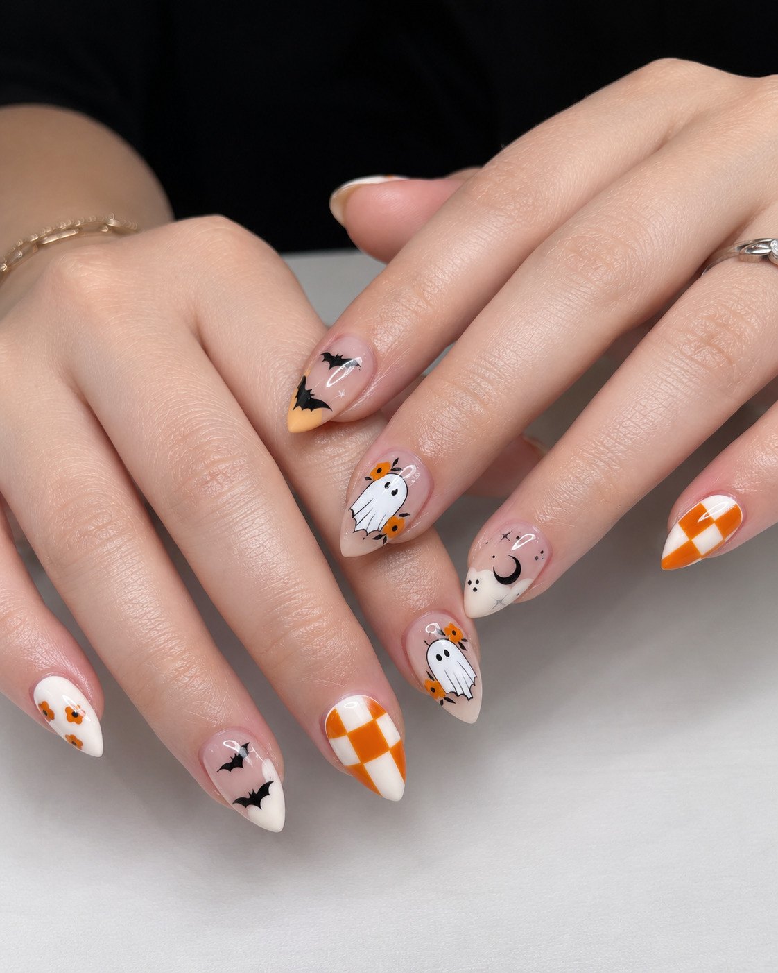 Almond Halloween nails with flower-framed ghosts, bats, a crescent moon and orange checkerboard