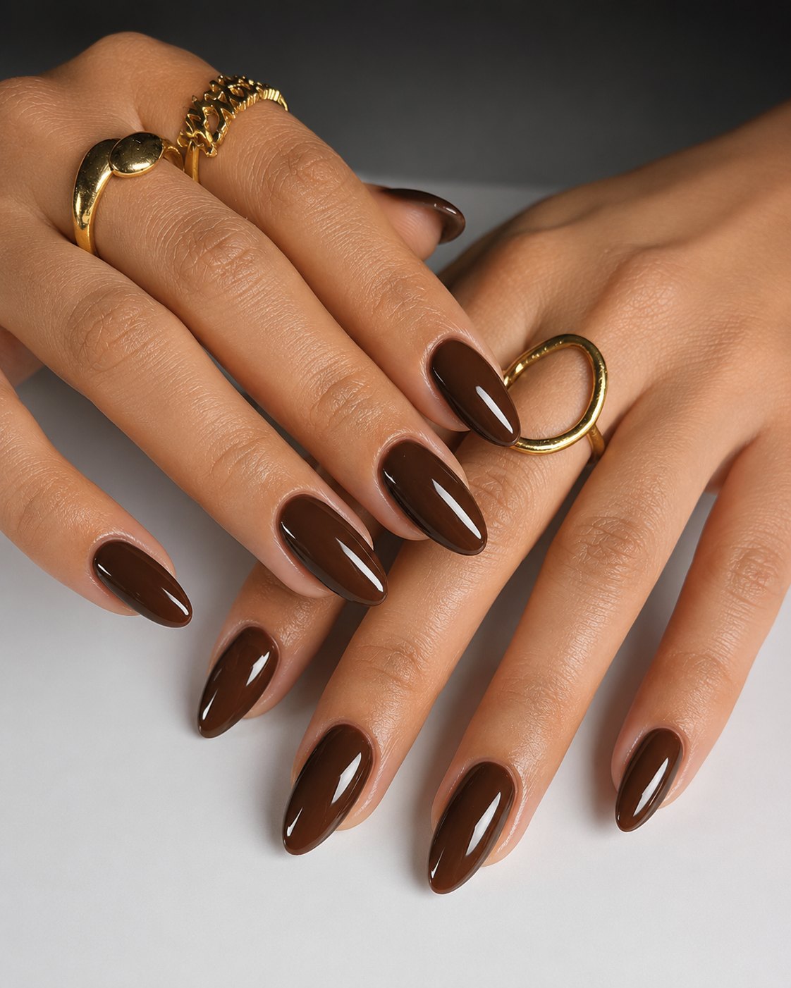 Glossy espresso brown almond nails on both hands with chunky gold rings