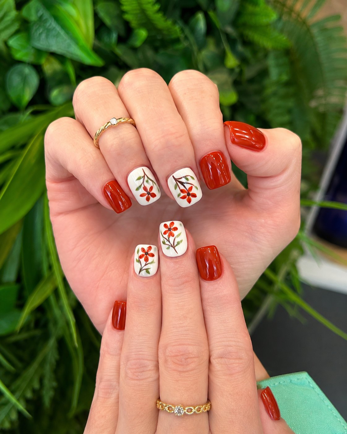 Short square homecoming nails in glossy brick red with hand-painted red daisies on white accent nails