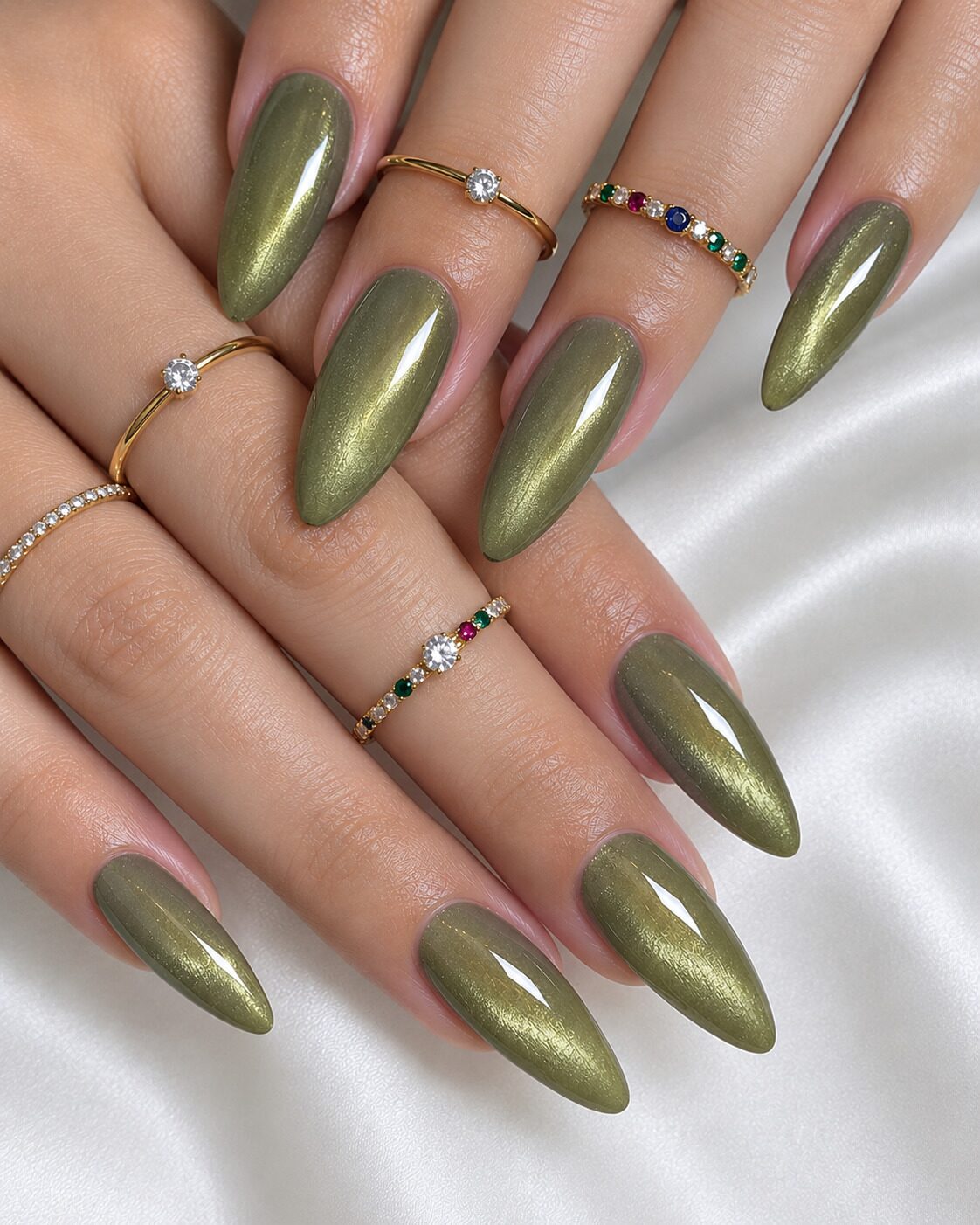 Long almond olive cat-eye nails with gold shimmer and gemstone stacking rings