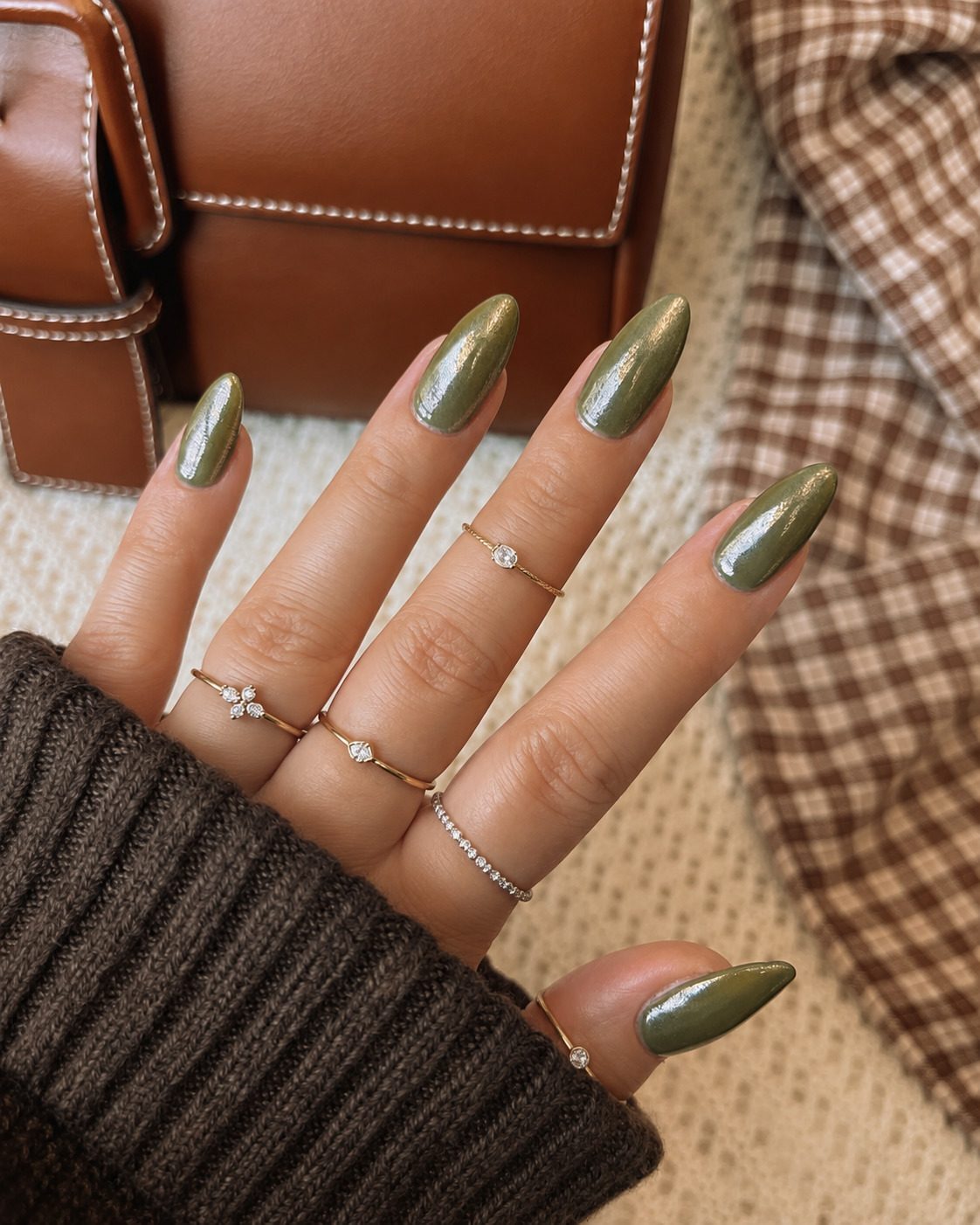 Glazed olive green nails with a pearly chrome finish and dainty gold rings