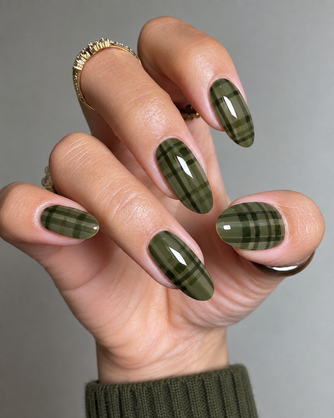 Sheer olive jelly almond nails with darker green plaid lines and a knit cuff