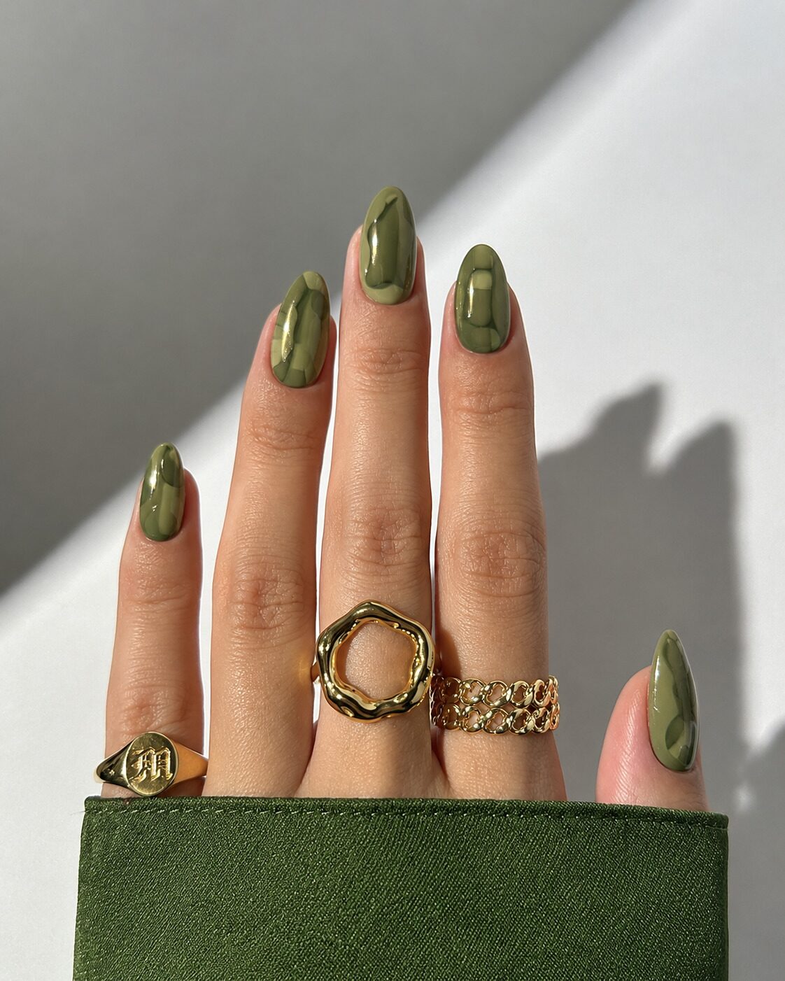 Glossy almond nails in tonal olive and sage camo patches with chunky gold rings
