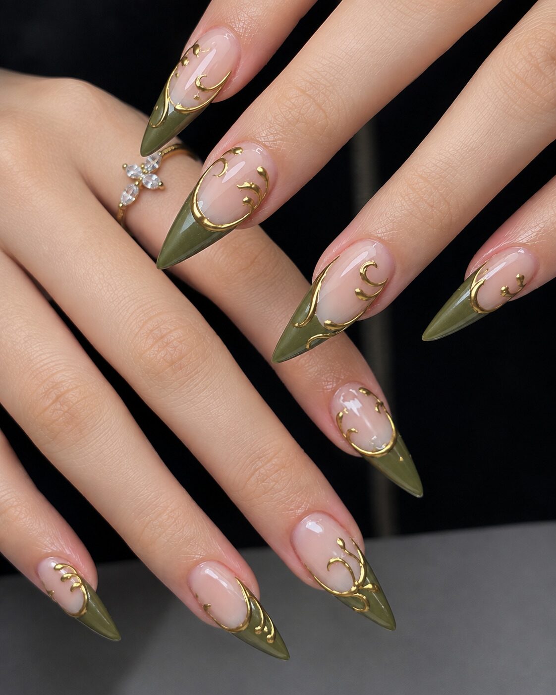 Long olive stiletto French tip nails with raised gold swirls on a black background
