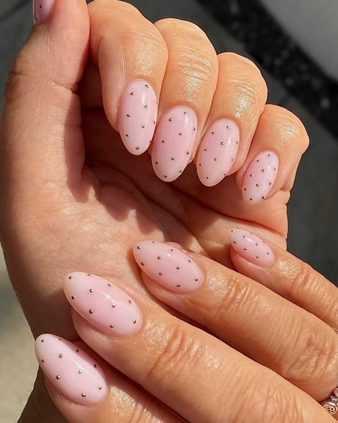 Polka dot nails with tiny metallic silver dots on a glossy light pink background for a minimalist chic look.