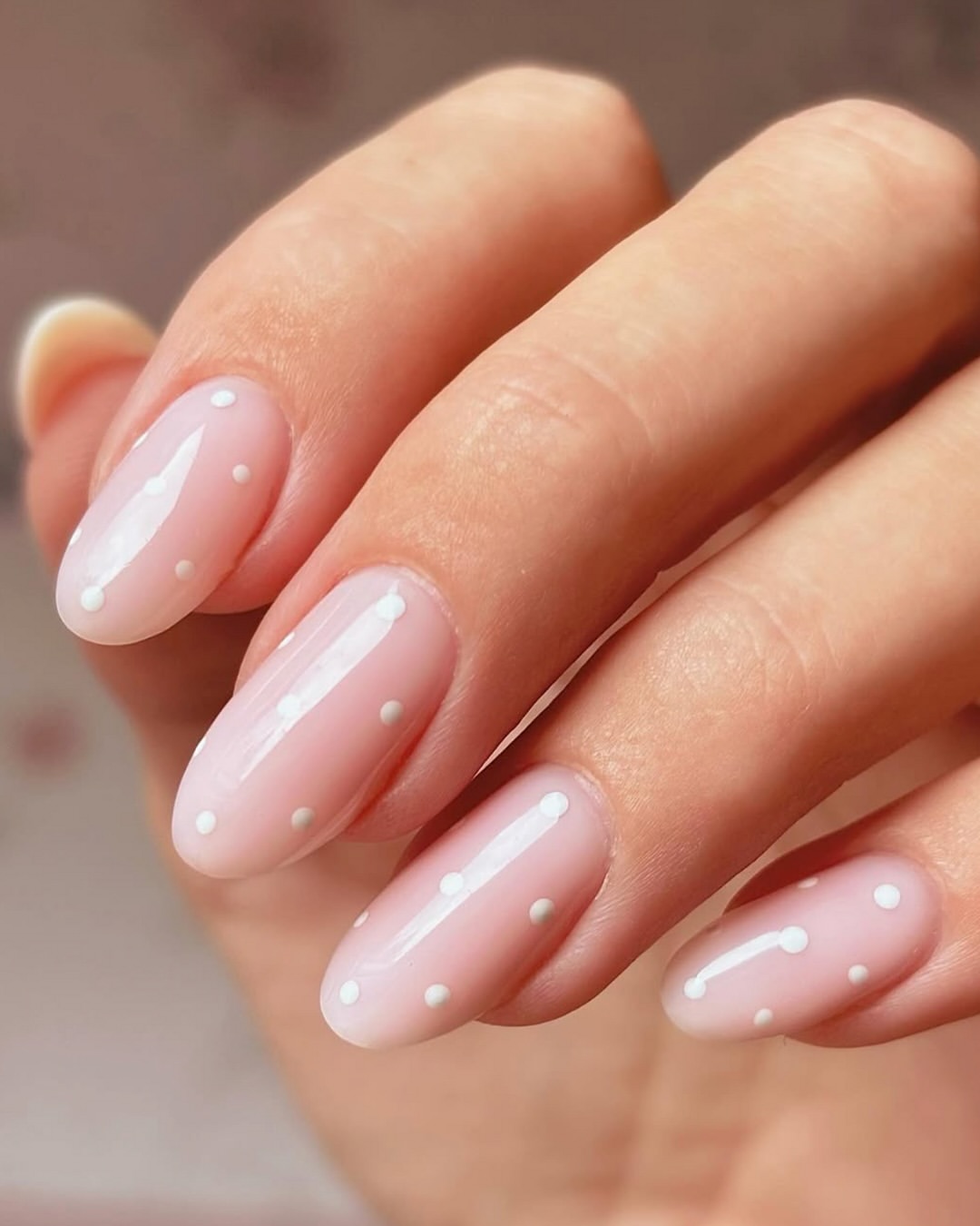 Polka dot nails with white dots on a sheer nude pink base in an elegant minimalist style.