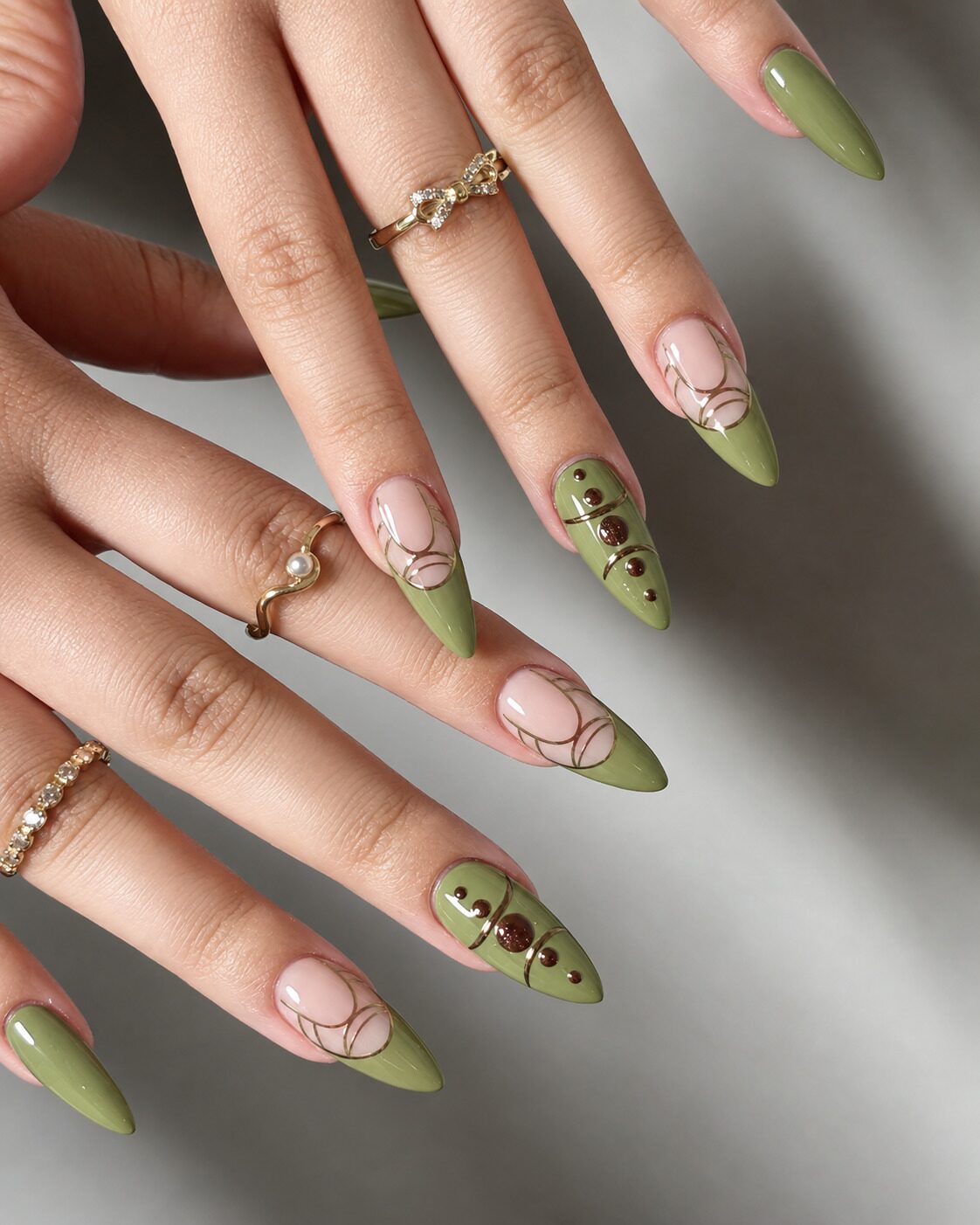 Sage green French tip almond nails with gold line arcs and brown dot accents