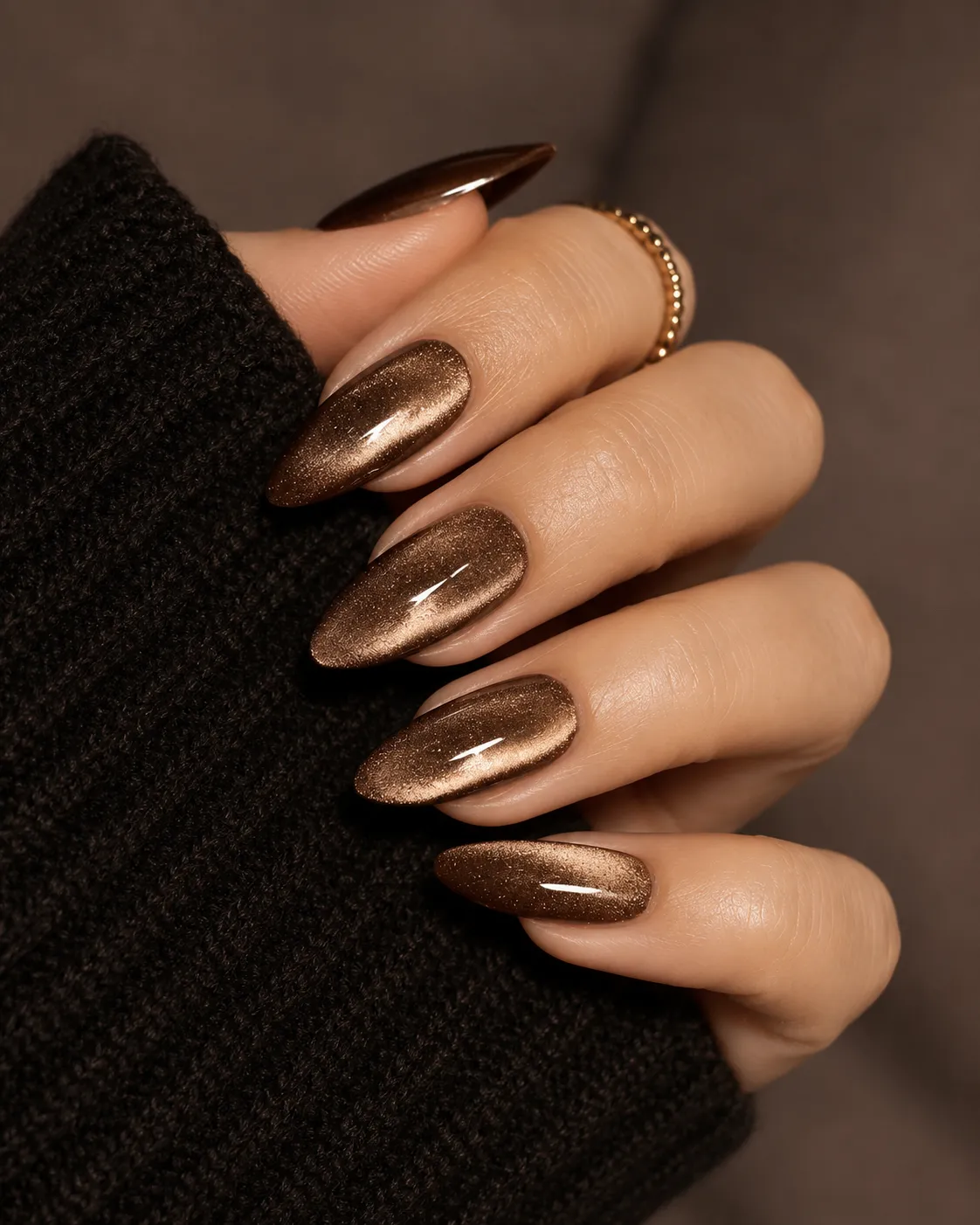 8 Ways to Wear Brown Nails This Season in Houston 3 Hand with long shimmery brown almond nails and a gold ring, wearing black sweater