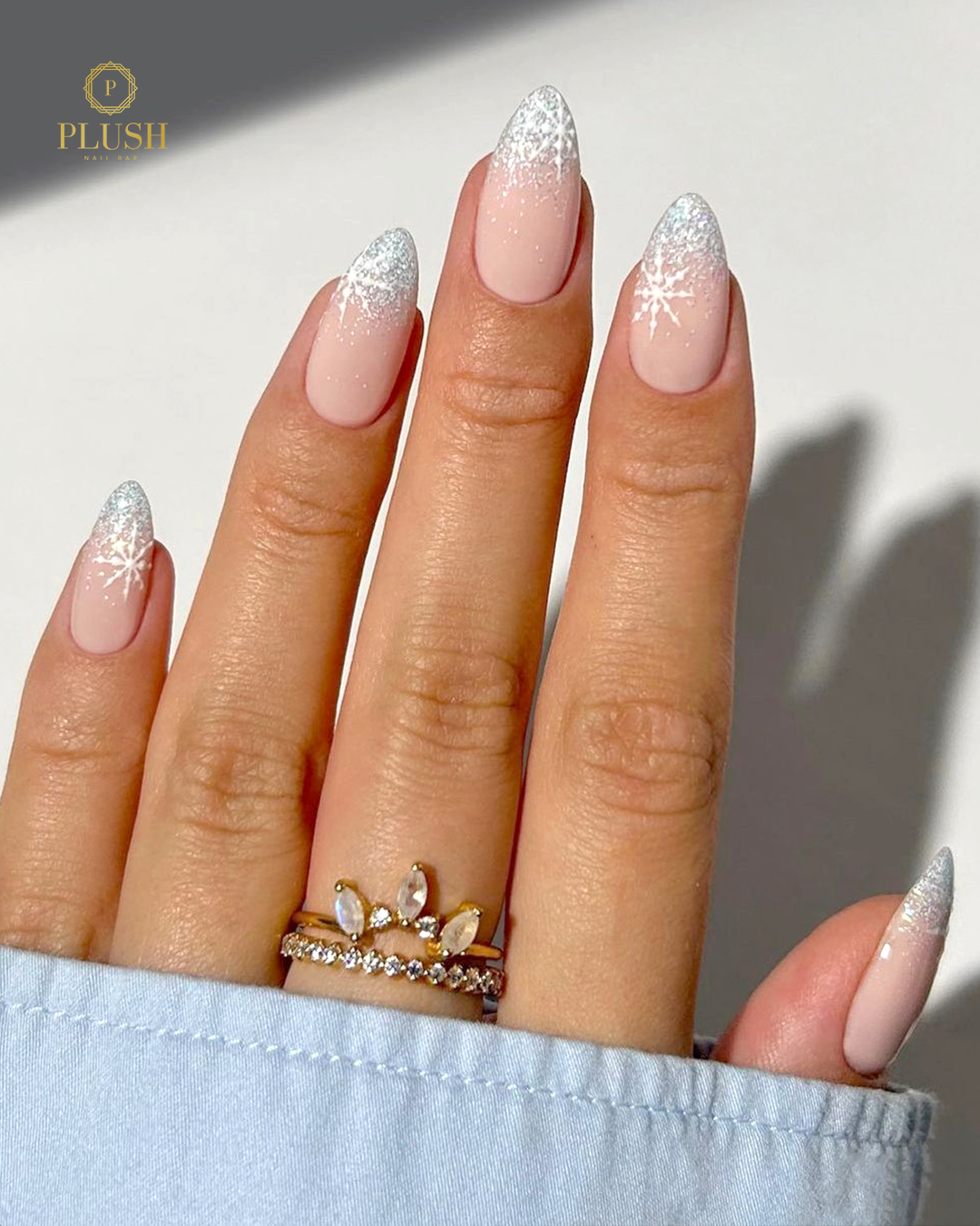 Almond nails with a soft pink base, silver glitter gradient, and delicate white snowflake designs.