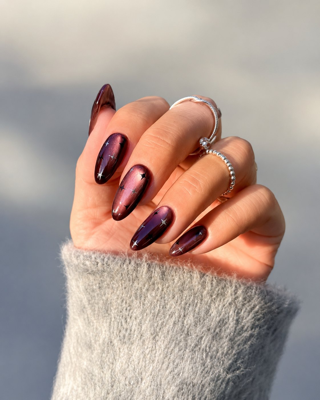 Dark plum cat-eye nails with tiny silver star decals