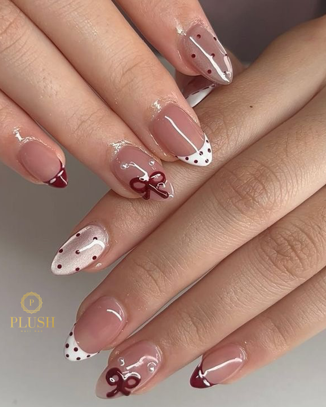 Neutral valentine nails with red bow and polka dot French tips at Plush Nail Bar